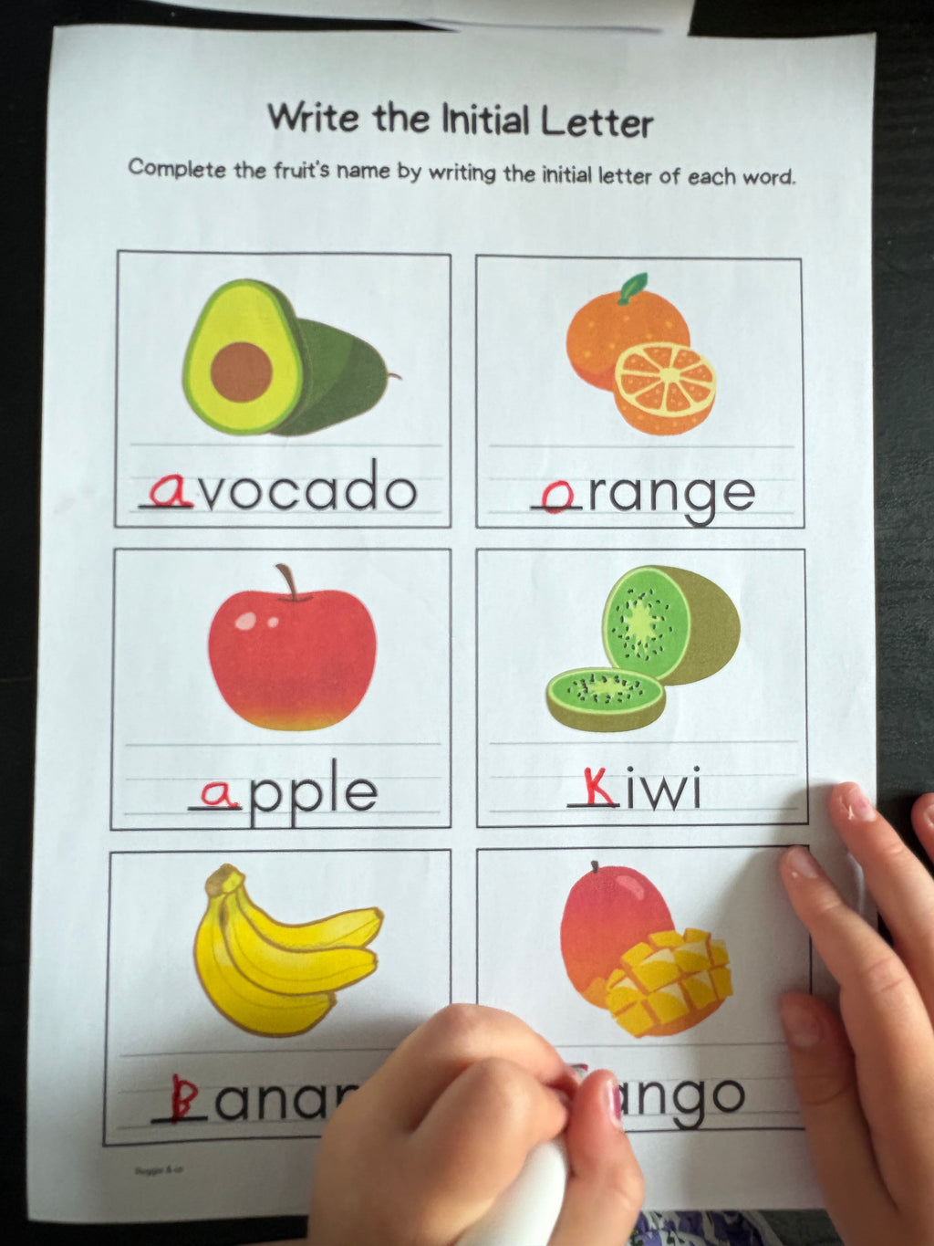 Educational worksheet with fruit images and labels, being used by a child.