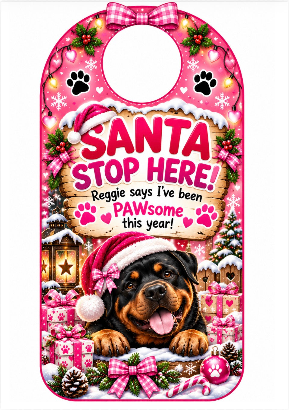 A pink Christmas-themed pet door bib with a Rottweiler dog illustration and the text 'SANTA STOP HERE! Reggie says I've been PAWsome this year!'. The bib features a festive design with a Santa hat, gifts, snow, paw prints, and a gingham bow at the top.