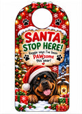 A personalized Christmas door hanger or luggage tag featuring a Rottweiler dog wearing a Santa hat, surrounded by festive holiday decorations and a custom text message that reads 'Santa Stop Here! Reggie says I've been PAWsome this year!'.