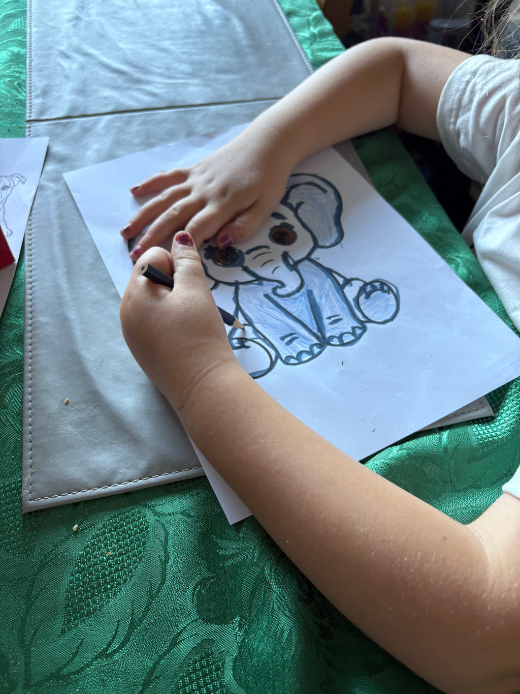 Child coloring a picture of an elephant on a green tablecloth.