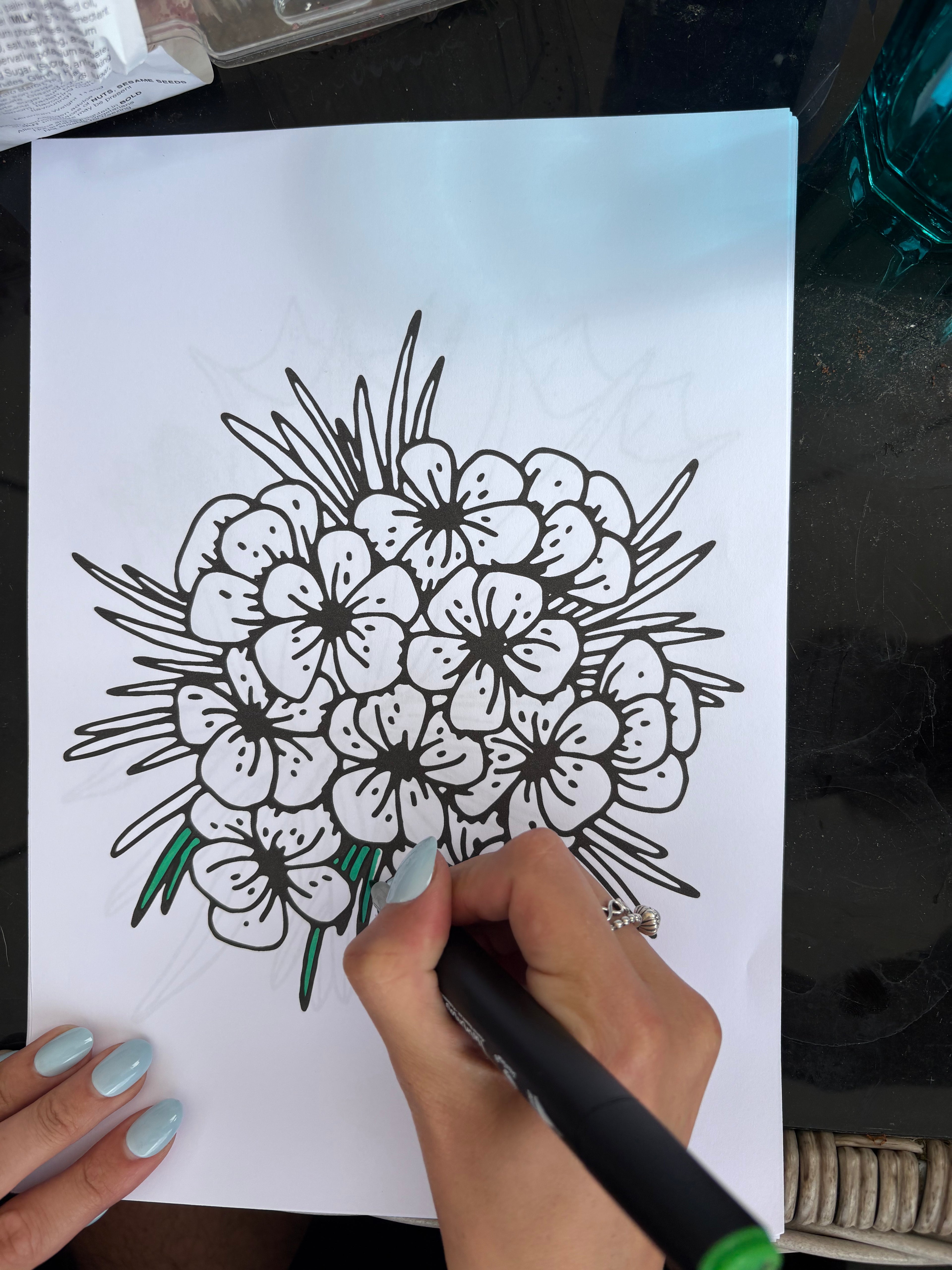 Hand drawing a floral design on white paper with a black marker.
