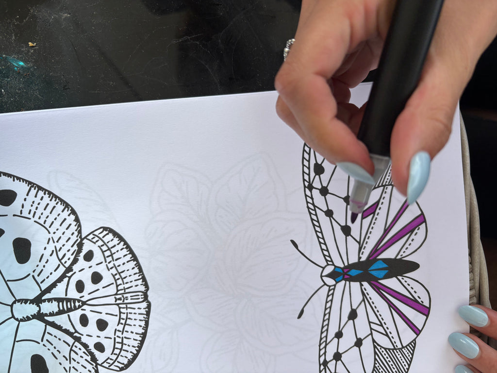 Hand holding a stylus over a drawing of a butterfly on a white sheet of paper.