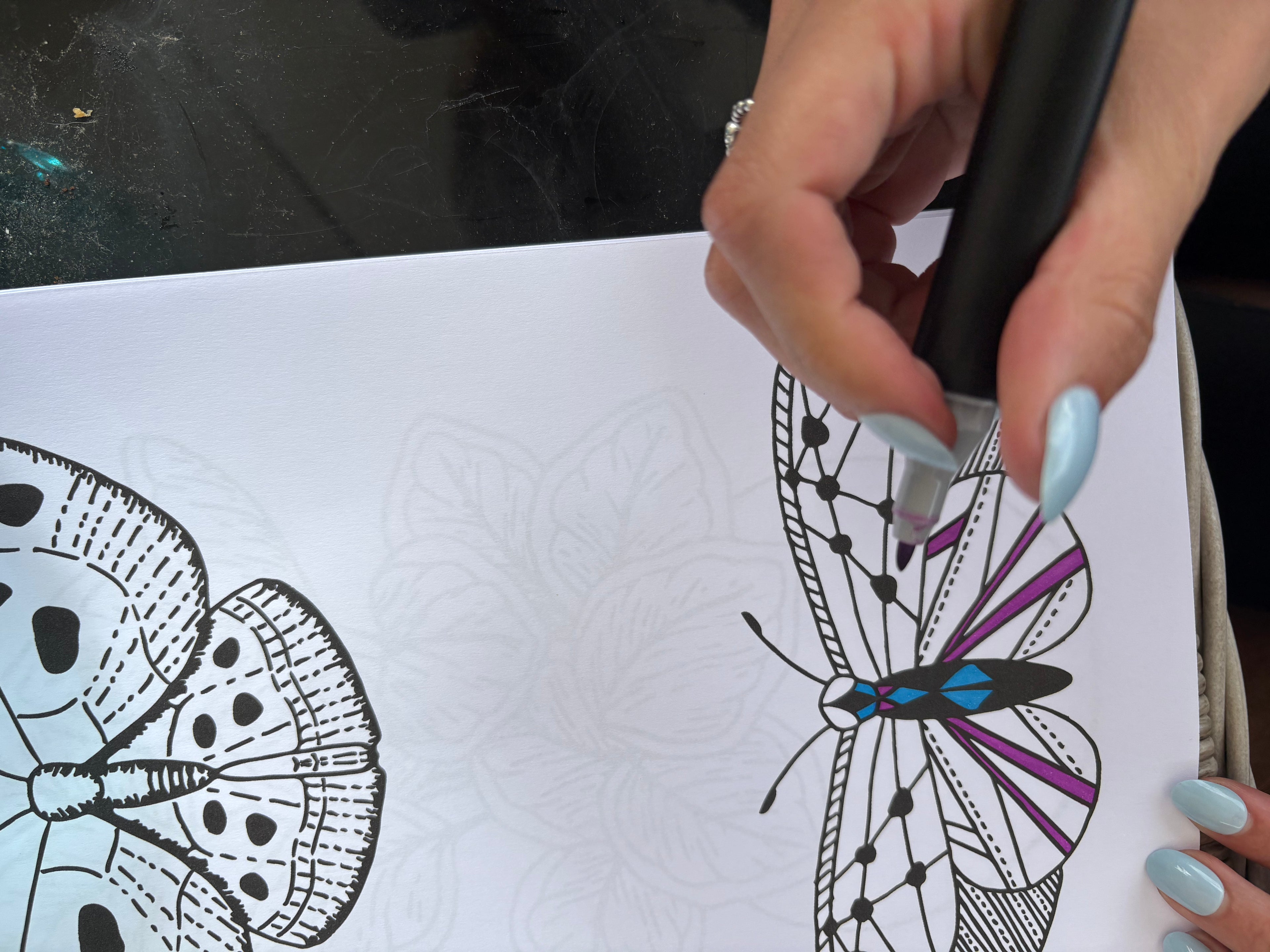 Hand holding a stylus over a drawing of a butterfly on a white sheet of paper.