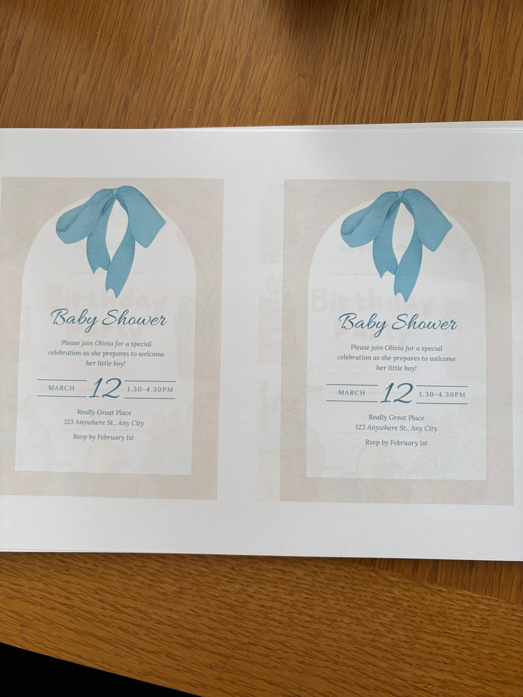 Two baby shower invitations with blue ribbons on a wooden surface
