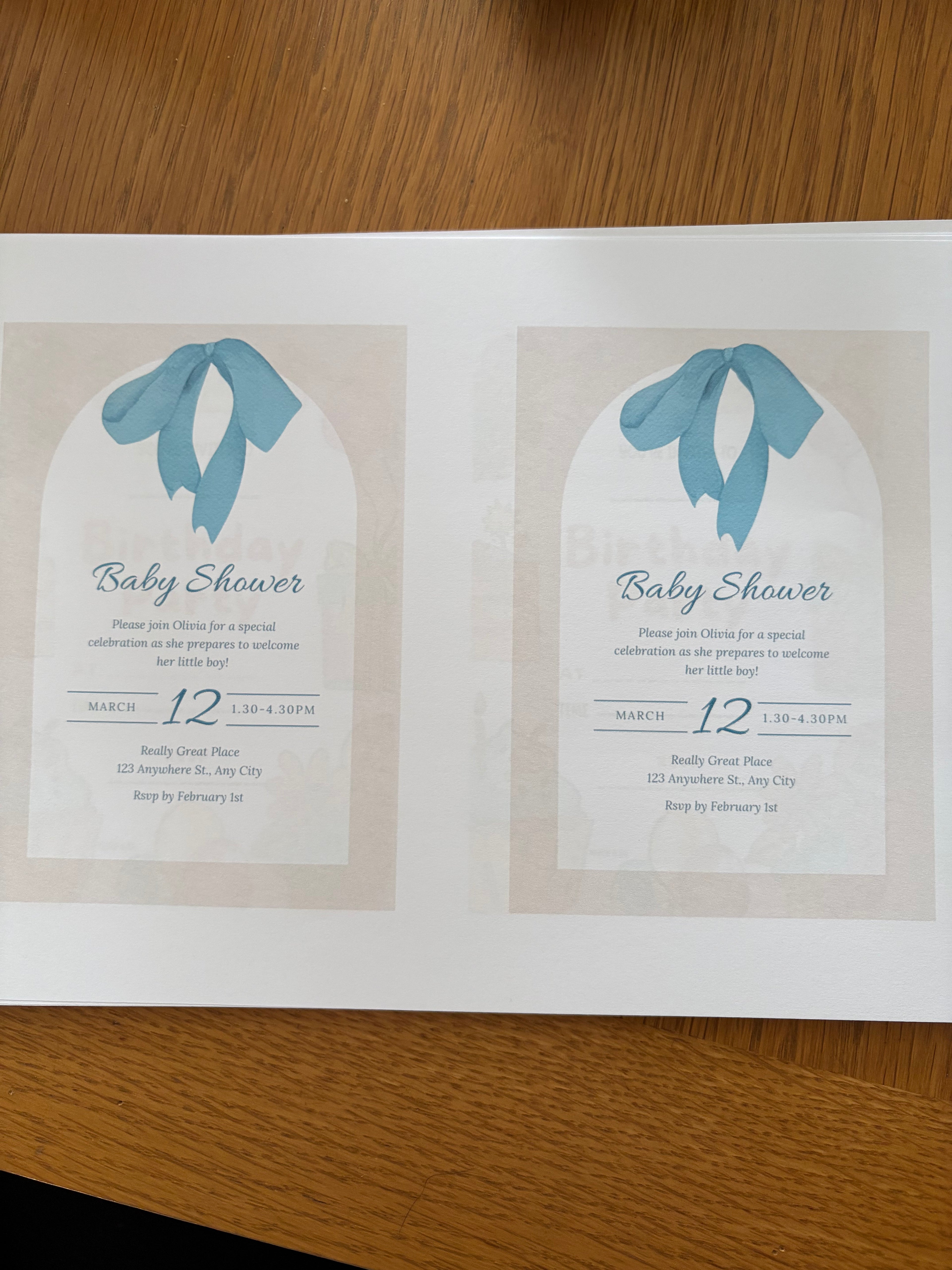 Two baby shower invitations with blue ribbons on a wooden surface