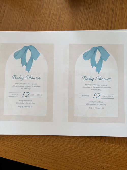 Two baby shower invitations with blue ribbons on a wooden surface